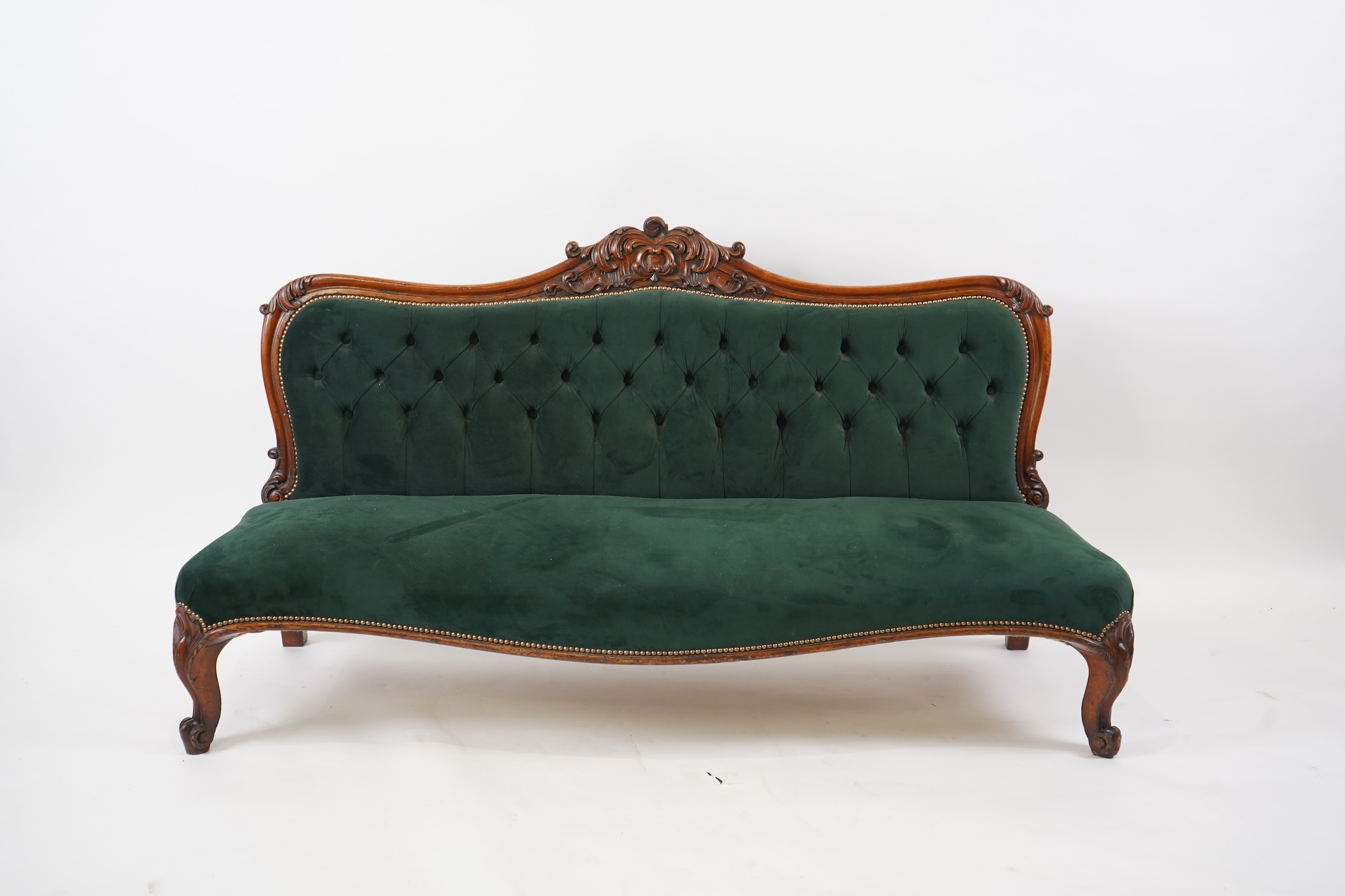 A pair of Victorian carved oak settees, recently re-upholstered in deep buttoned green velvet, the scroll carved crest rails over serpentine seats on cabriole front legs, 160cm wide, 96cm high, Provenance - previously gi